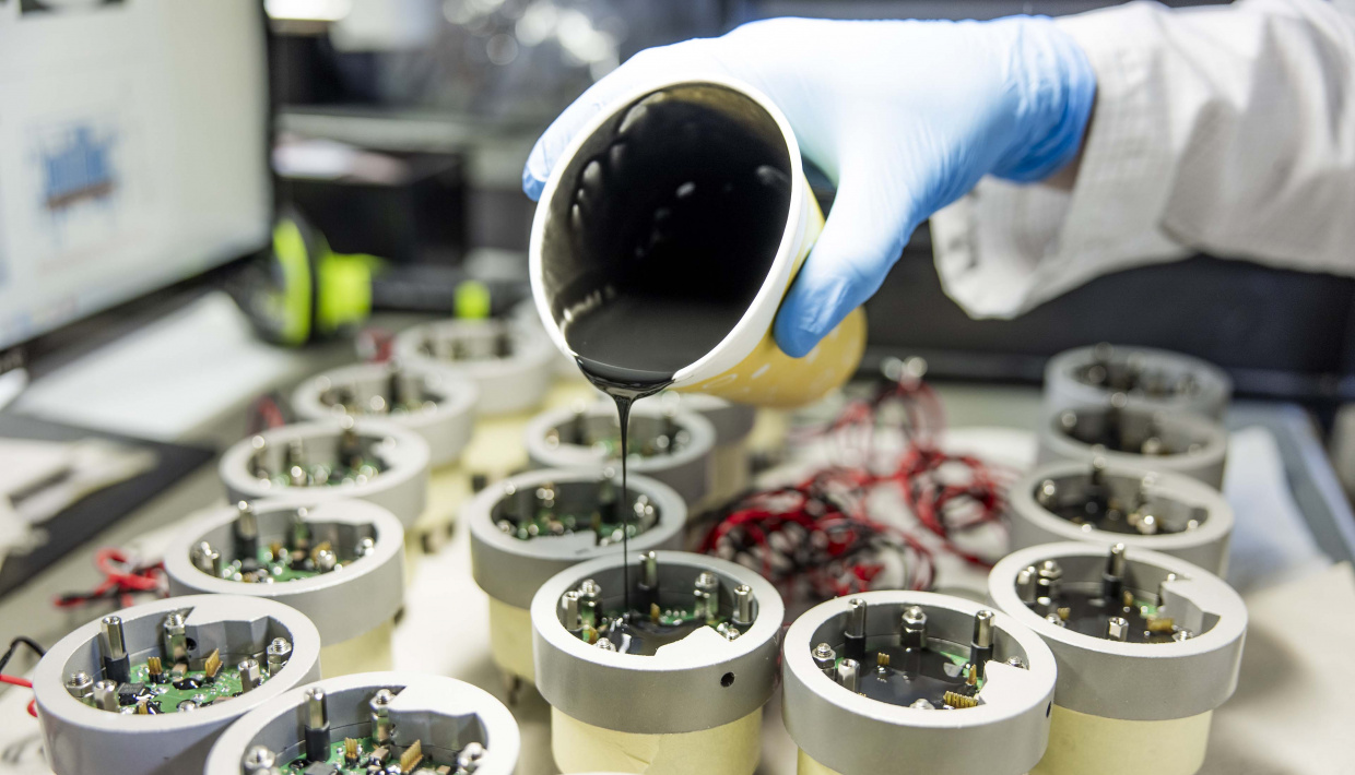 Un liquide noir coule d'un gobelet sur des contenants avec des composants électroniques